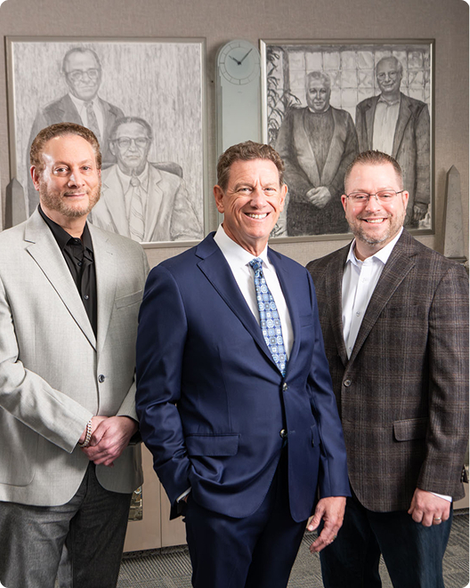 Merit Brass senior leadership team standing in front of company founder portraits